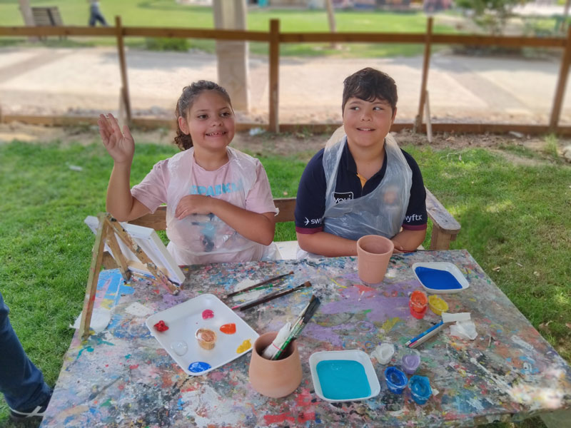 Children doing an outdoor art activity together — painting a canvas and a pot as part of a sensory-friendly, inclusive family travel experience.