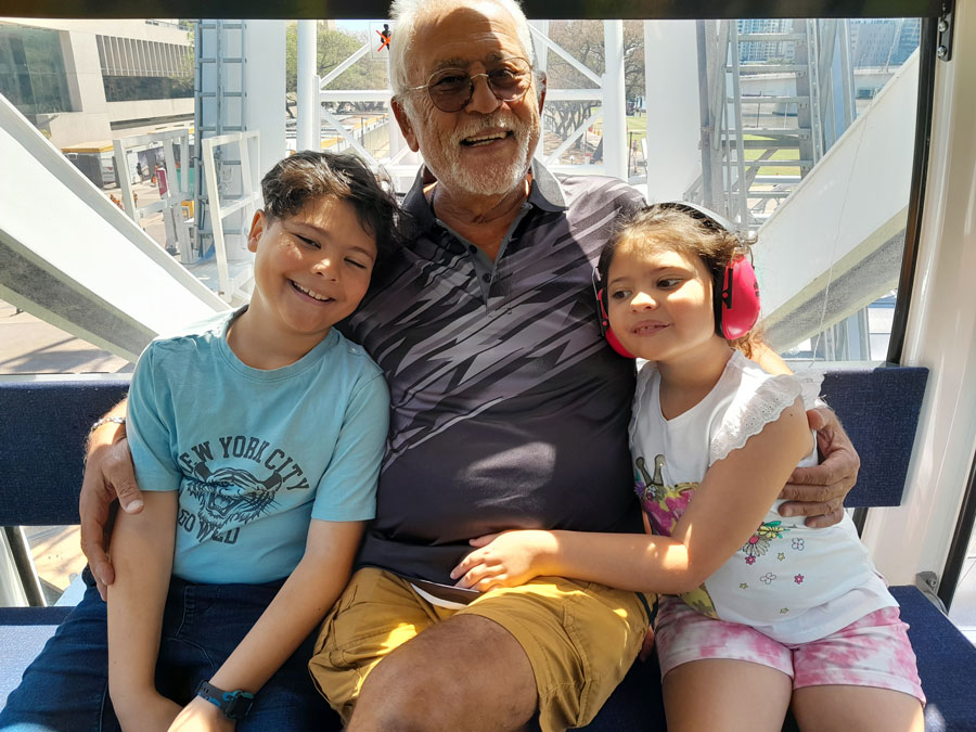 A grandfather and his two grandchildren happily smiling as they take in the sights on a ferris wheel