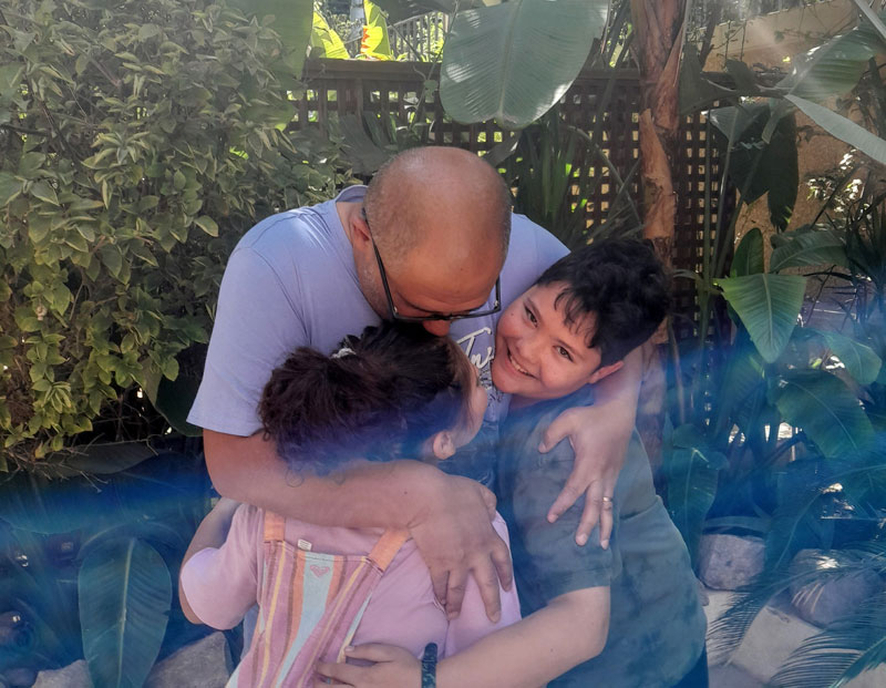 Father hugging his son and daughter while sun is bathing them outside in a garden