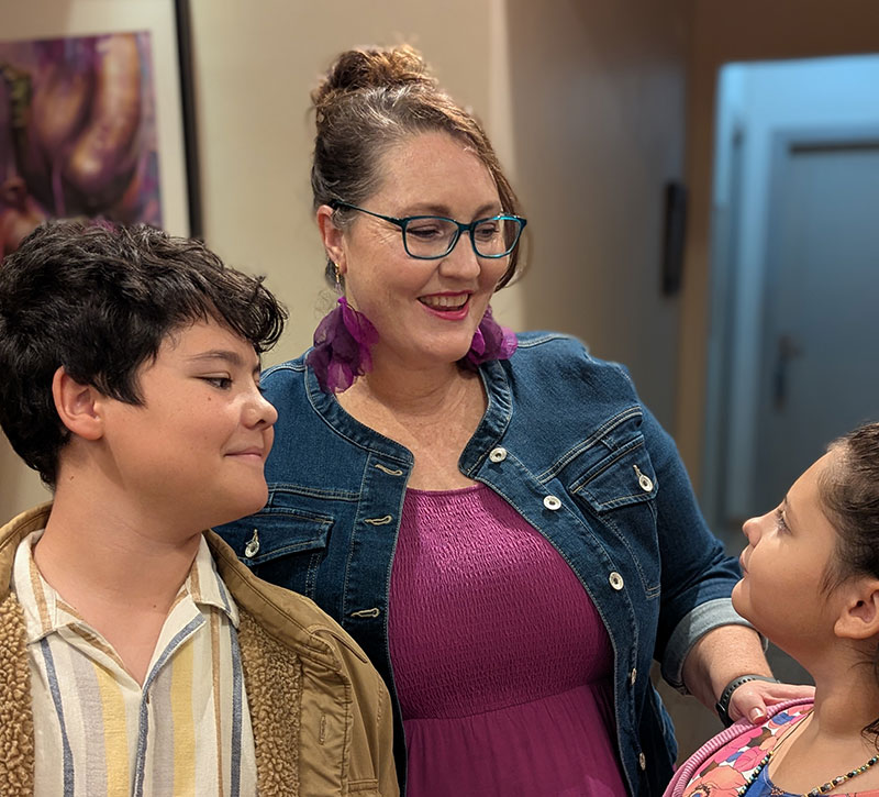 Mother smiling down at daughter who is looking up at her and son looking on