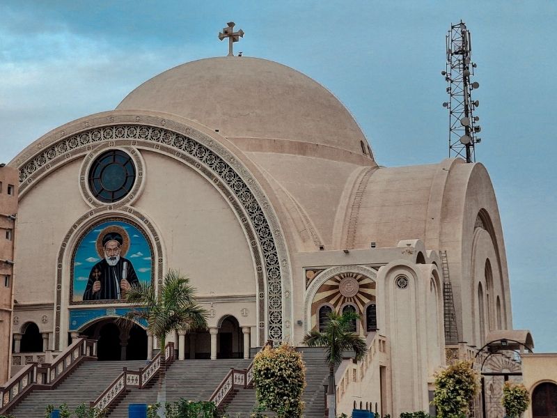 Domed building with a cross on top and stairs leading up to it and a religious painting on the front
