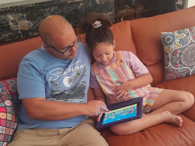 Father and daughter sitting on the couch cuddling while watching an iPad together