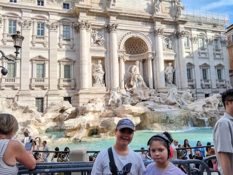 Trevi Fountain A young boy and girl standing in front of the Trevi Fountain in Rome, with crowds. The girl is wearing ear defenders.