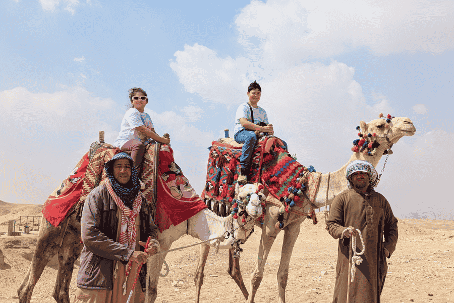 A girl and a boy riding camels in the desert at Saqqara with guides leading them